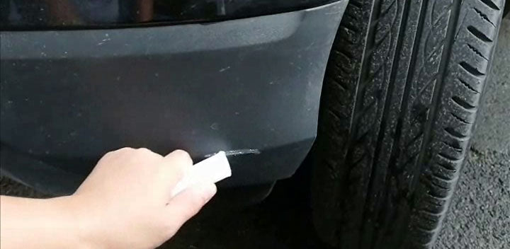 A black plastic bumper with visible scratches being sanded down with a fine grit sandpaper.